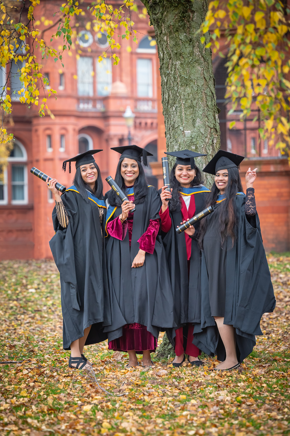 Four graduates stood under a tree outside the Peel Building