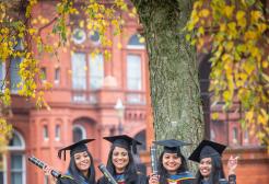 Four graduates stood under a tree outside the Peel Building 